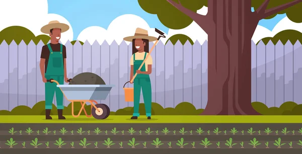 ホーとバケツアフリカ系アメリカ人カップル農家を持つ地球の女性の手押し車を持つ庭師の男は、完全な長さの裏庭の背景水平 — ストックベクタ