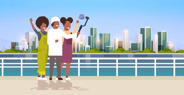 Περιστασιακή άτομα που χρησιμοποιούν 3-άξονα σταθεροποιητή τοποθέτησης selfie stick για το smartphone Happy Αφρικανών Αμερικανών τουριστών λήψη φωτογραφία στέκεται μαζί πάνω από το φόντο της πόλης οριζόντια πλήρες μήκος — Διανυσματικό Αρχείο