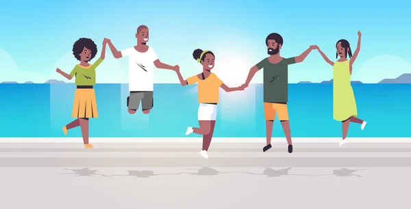 Молодые люди группа прыжки на пляже мужчины женщины держась за руки летние каникулы концепция африканских американских друзей, веселые морские каникулы путешествие полный горизонтальный — стоковый вектор
