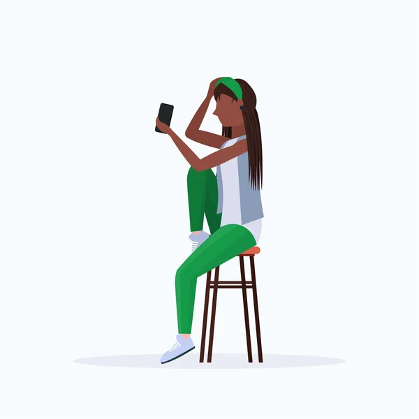 Mujer tomando foto selfie en el teléfono inteligente cámara afroamericana personaje de dibujos animados femeninos sentado en la silla posando sobre fondo blanco plana de longitud completa — Vector de stock