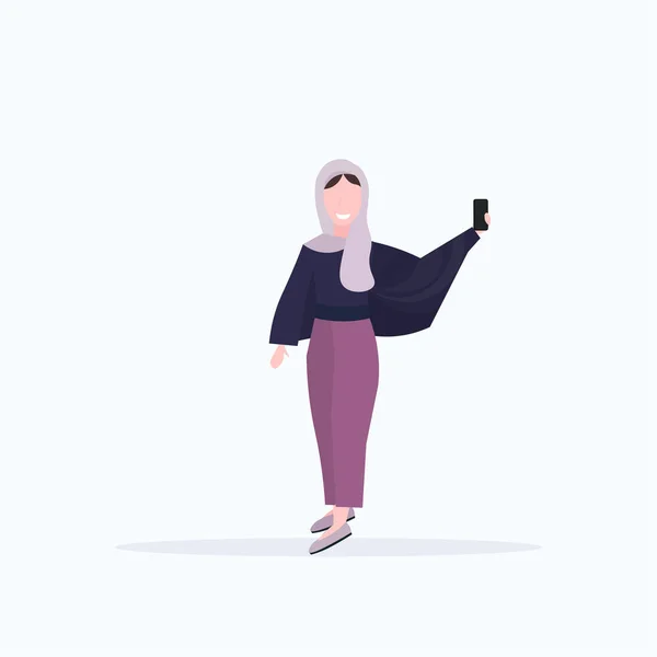 Mulher em lenço de cabeça tirar foto selfie no smartphone câmera árabe personagem de desenho animado feminino posando fundo branco plana comprimento total — Vetor de Stock