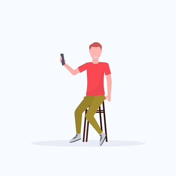 Hombre tomando foto selfie en la cámara del teléfono inteligente personaje de dibujos animados masculinos casual sentado en la silla posando fondo blanco de longitud completa plana — Vector de stock