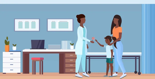 Mor med dotter besöker African American doktor barnläkare ger Lollipop till liten flicka samråd sjukvård Concept modern sjukhus interiör full längd Flat horisontell — Stock vektor