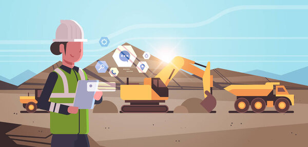 open pit woman worker in helmet using mobile app excavator loading soil on dump truck professional equipment working on coal mine production opencast stone quarry background portrait horizontal