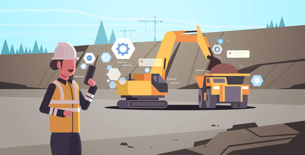 woman in helmet using walkie talkie controlling excavator loading soil on dump truck professional equipment working on coal mine production opencast stone quarry background portrait horizontal