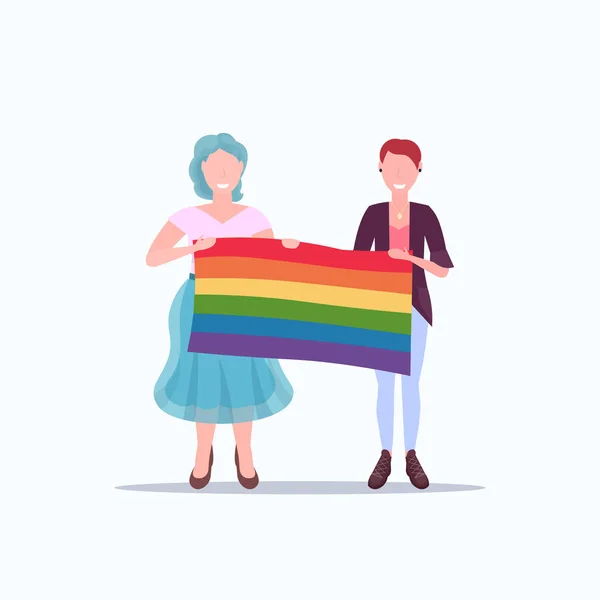 Kvinnor par Holding Rainbow Flag kärlek parad hbt Pride Festival Concept två lesbiska leende kvinnliga seriefigurer stående tillsammans full längd platt — Stock vektor
