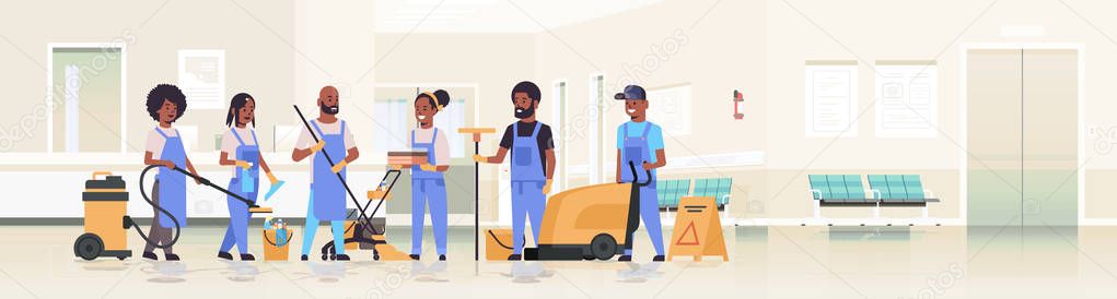 cleaners team in uniform working together cleaning service concept african american janitors using professional equipment clinic reception hospital corridor interior flat full length horizontal