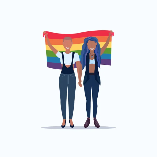 Donne coppia tenendo bandiera arcobaleno amore parata lgbt orgoglio festival concetto mix gara lesbica femminile personaggi dei cartoni animati in piedi insieme a tutta la lunghezza piatta — Vettoriale Stock