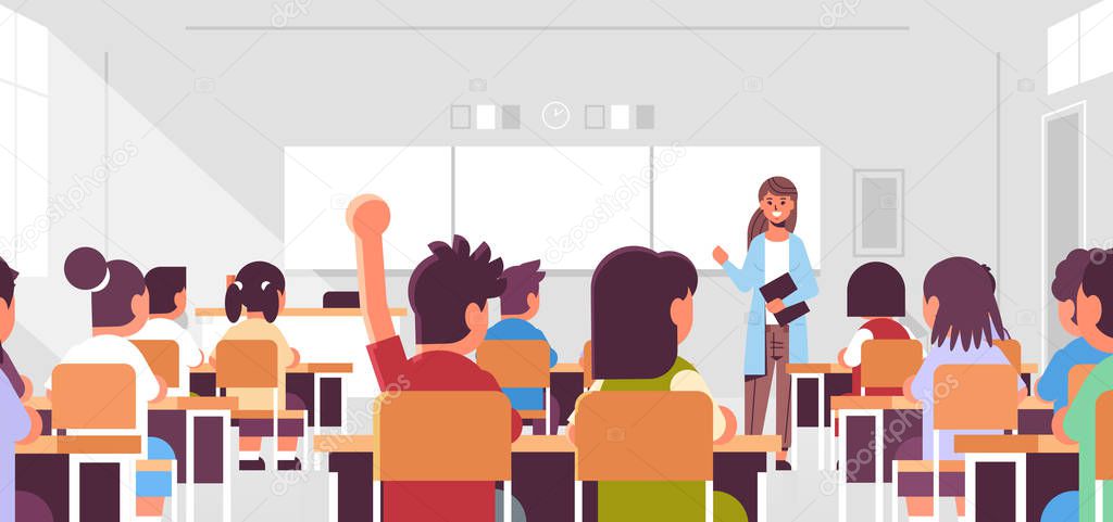 pupils group listening to female teacher schoolboy raising hand to answer in classroom during lesson teaching education concept modern class room interior flat horizontal portrait