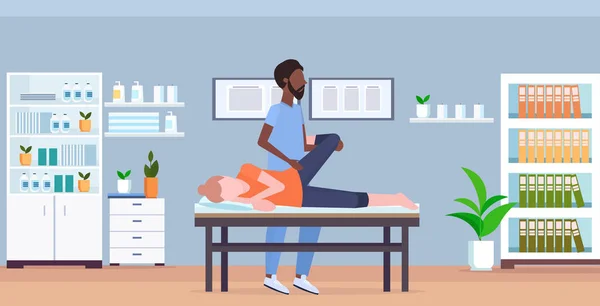 Девушка лежит на массажной кровати африканский массажист-терапевт делает лечебное лечение массируя ноги пациента ручная физиотерапия концепция медицинской клиники интерьер кабинета всю длину — стоковый вектор