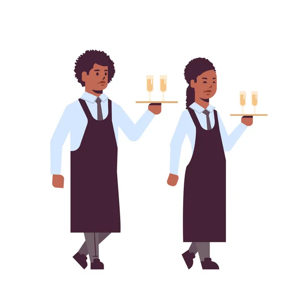 Professionele obers Holding serveren trays met glazen champagne African American man vrouw restaurant werknemers in uniform dragen alcohol dranken platte volledige lengte witte achtergrond — Stockvector