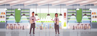 profesyonel garsonlar çift sıcak misafirperverliği modern kafe iç düz tam uzunlukta yatay gösteren önlük rahat restoran kadın erkek işçilere karşılama menüsü tutan