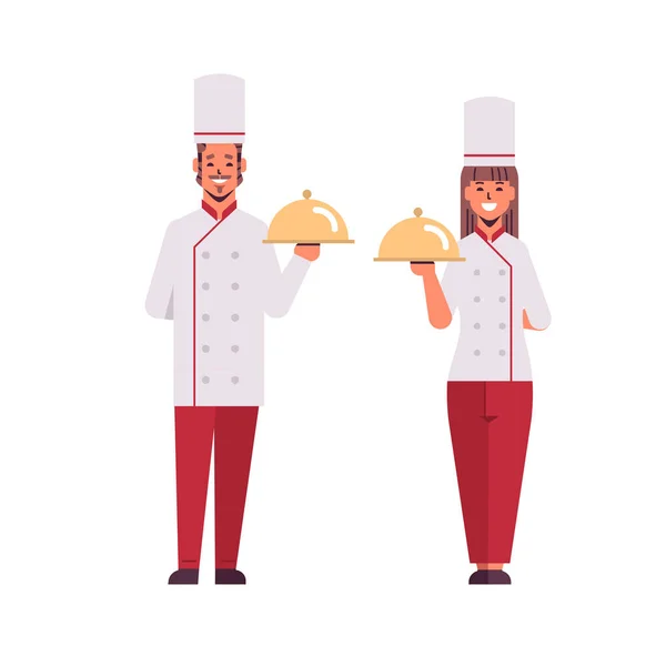 Cooks couple professional chefs holding covered platters serving trays woman man restaurant workers in uniform standing together cooking food concept flat full length — Stock Vector