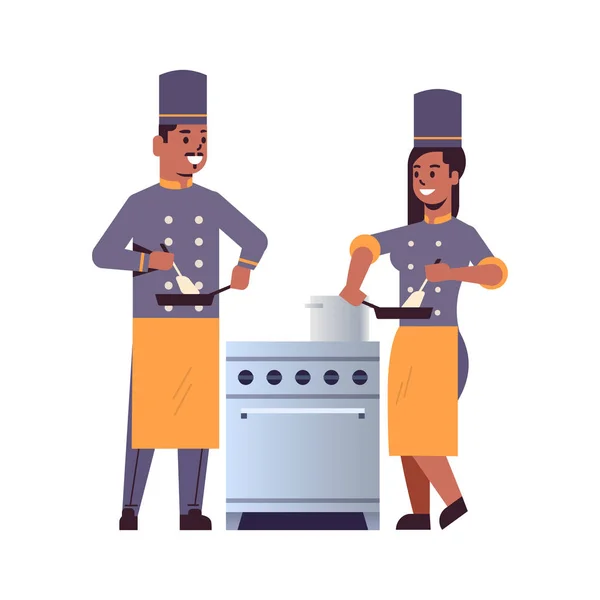 Cocina pareja de chefs profesionales utilizando sartén revolviendo comida afroamericana hombre mujer restaurante cocina trabajadores en uniforme de pie juntos cerca de la estufa concepto de cocina plana de longitud completa — Vector de stock
