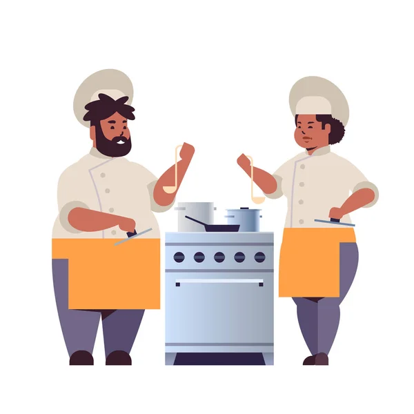 Cooks couple professional chefs preparing and tasting dishes african american woman man restaurant workers in uniform standing together near kitchen stove cooking food concept flat full length — Stock Vector