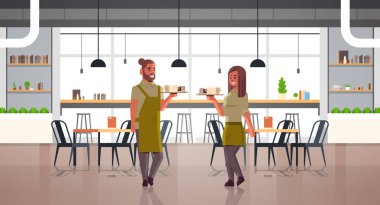 garsonlar çift tepsi adam kadın kafe işçileri üzerinde kahve ve kek taşıyan aprons tatlılar modern kafeterya iç tam uzunlukta yatay cappuccino bardak tutan