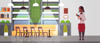 profesyonel garson şarap şişesi tutan afro-amerikan kadın restoran işçisi kırmızı önlük alkol içki modern kafe iç düz tam uzunlukta yatay sunan