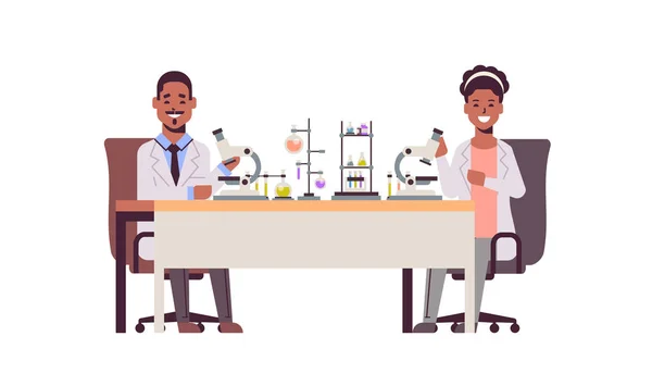Científicos pareja usando microscopio africano americano hombre mujer en uniforme sentado a la mesa haciendo experimentos científicos en laboratorio de química con tubos de ensayo investigación ciencia concepto longitud completa — Vector de stock