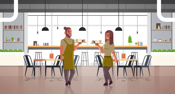 Garsonlar çift tepsi adam kadın kafe işçileri üzerinde kahve ve kek taşıyan aprons tatlılar modern kafeterya iç tam uzunlukta yatay cappuccino bardak tutan — Stok Vektör