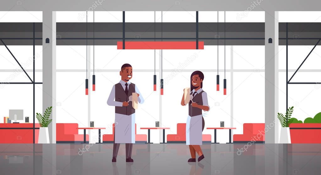 professional waiters couple polishing wine glass with towel african american man woman restaurant workers in uniform modern cafe interior flat full length horizontal