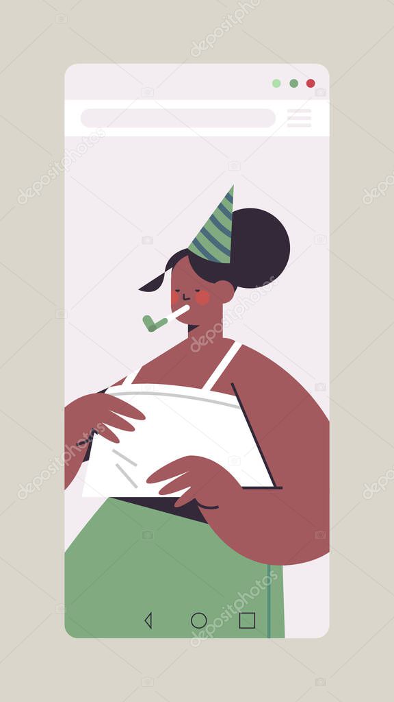 woman in festive hat celebrating online birthday girl in smartphone screen blowing in party blower