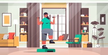 Kadın, evdeki platformda dambıllarla egzersiz yapıyor. Kardiyo fitness eğitimi alıyor.