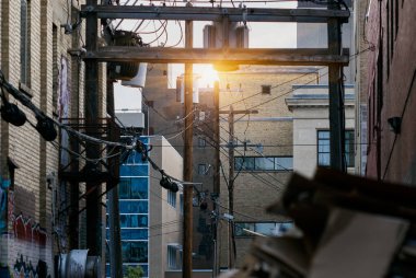 Kanada, Saskatoon 'da şehir merkezinde elektrik direklerini, elektrik hatlarını, trafoları ve modern cam mimariyle eski tuğla duvarların karışımını gösteren manzaralı bir manzara. Sahne altyapı ve şehir tasarımının zıtlığını vurguluyor.