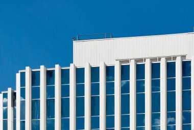 Kanada 'nın Saskatoon şehrindeki modern bir gökdelenin düşük açılı görüntüsü, açık mavi gökyüzü altında dikey cam pencereleri ve geometrik tasarımı olan beyaz cephe.