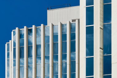 Kanada 'nın Saskatoon şehrindeki modern bir gökdelenin düşük açılı görüntüsü, açık mavi gökyüzü altında dikey cam pencereleri ve geometrik tasarımı olan beyaz cephe.