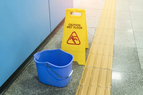 Señal de suelo húmedo de precaución amarilla en suelo húmedo con cubo azul — Foto de Stock