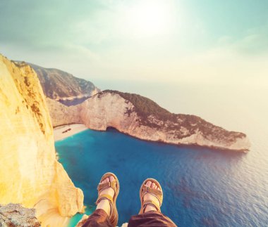 Denizin üzerindeki yüksek bir kayalıkta oturan kız. Seyahat konsepti.