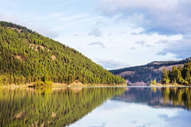 Sakin sulardaki kayaların yansımasıyla dağdaki gölün sakin manzarası..