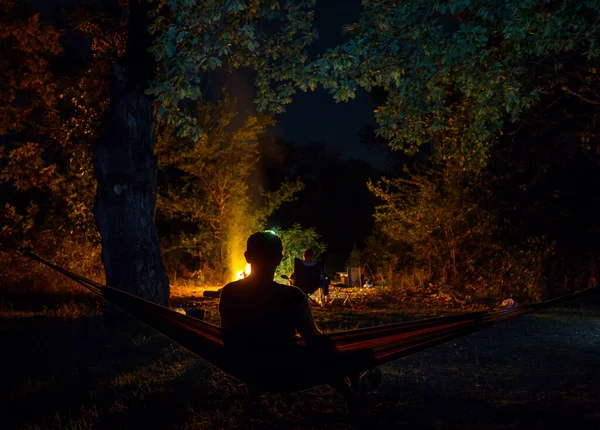 夜のキャンプで素晴らしいシーン 男でハンモックでたき火の背景 — ストック写真