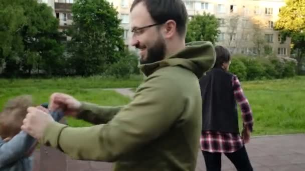 Adorable divertido juego de bebé en el patio de recreo bajo el cuidado de sus padres hipster — Vídeo de stock