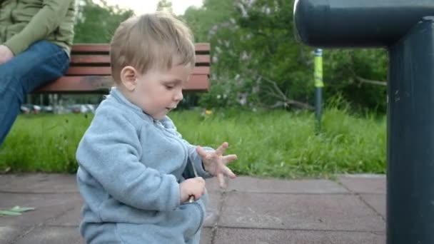 Чарівна смішна дитина грає на дитячому майданчику під опікою своїх батьків-хіпстерів — стокове відео