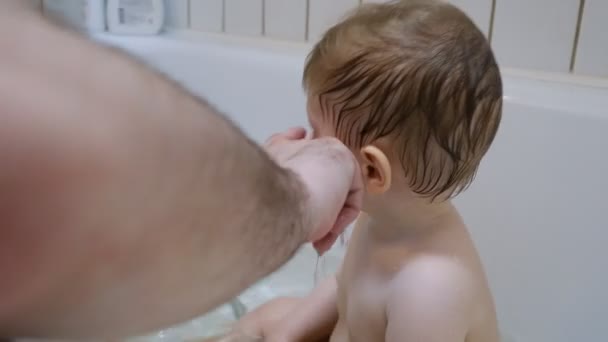 Очаровательный каштановые глаза младенца мыть в ванной с помощью своих родителей — стоковое видео