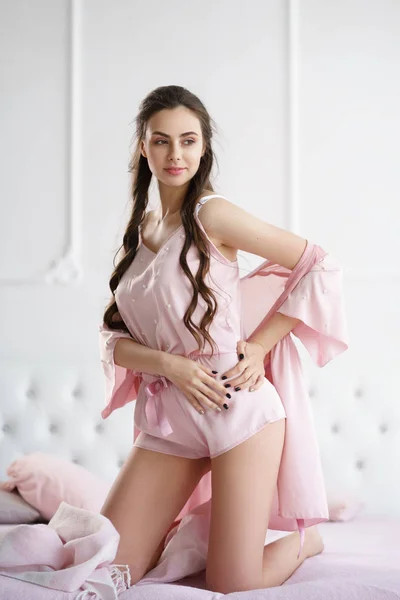 Красивая молодая женщина чувственно улыбается на кровати, играя с розовым набором пижамы — стоковое фото