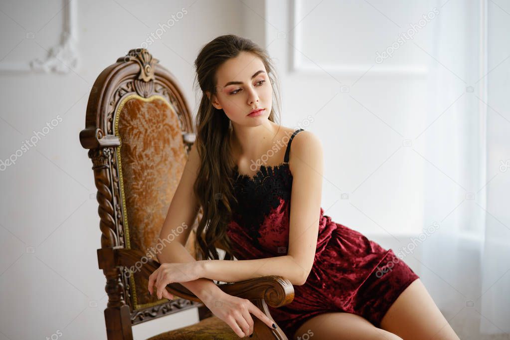 Beautiful young woman sitting on a vintage armchair in red pajama set