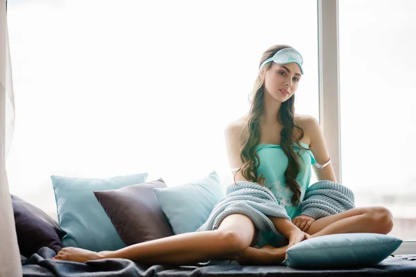 Piękna młoda kobieta siedzenia na poduszki okienne w turkusowy zestaw piżamy — Zdjęcie stockowe