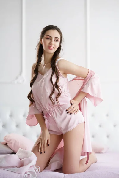 Krásná mladá žena se smyslně usmívala na posteli a hrála si s růžovým pyžamovou sadou — Stock fotografie