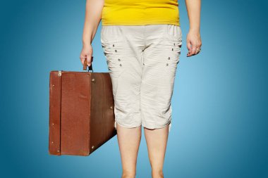 Sarı tişörtlü kadın elinde bir bavulla duruyor.