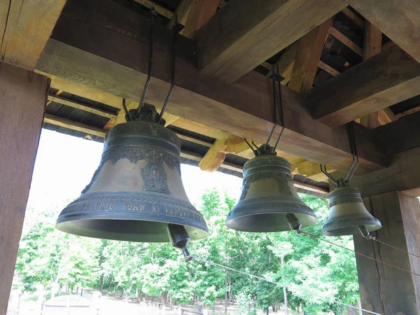 Bronze bells on brown wooden beams in church bell tower.