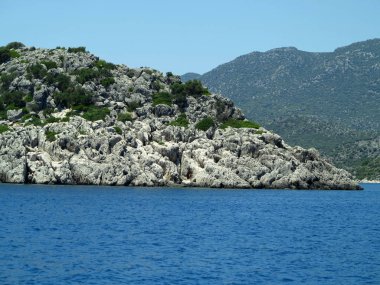 Mavi gökyüzü üzerinde yüksek kaya dağları ve deniz