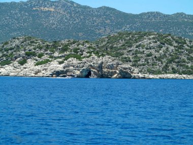 Mavi gökyüzü üzerinde yüksek kaya dağları ve deniz