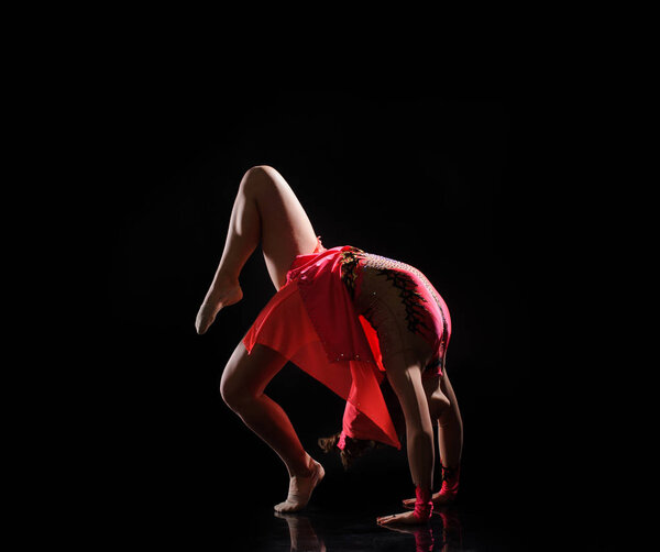 Young beautiful dancer gymnastics jumping in studio over black background