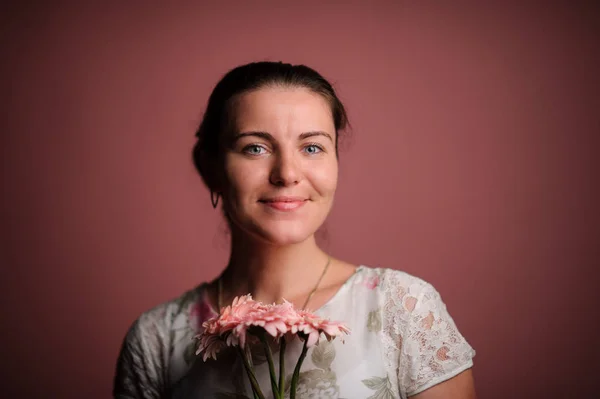 Lächelnde Frau mit rosa Blumen. Studio rosa Hintergrund — Stockfoto