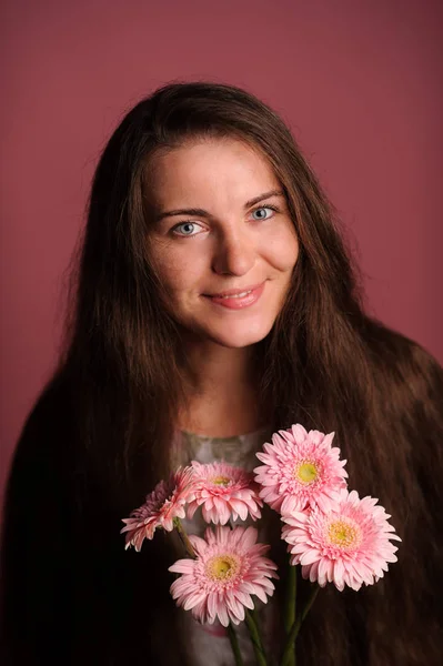 Glimlachende vrouw met roze bloemen. Studio roze achtergrond — Stockfoto