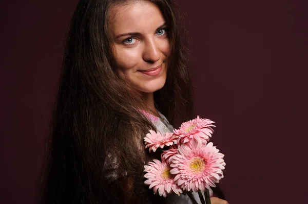 ピンクの花を持つ笑顔の女性。スタジオピンクの背景 — ストック写真