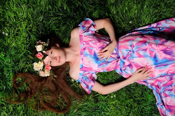 Jonge vrouw in de krans van folwers op een groen gras — Stockfoto