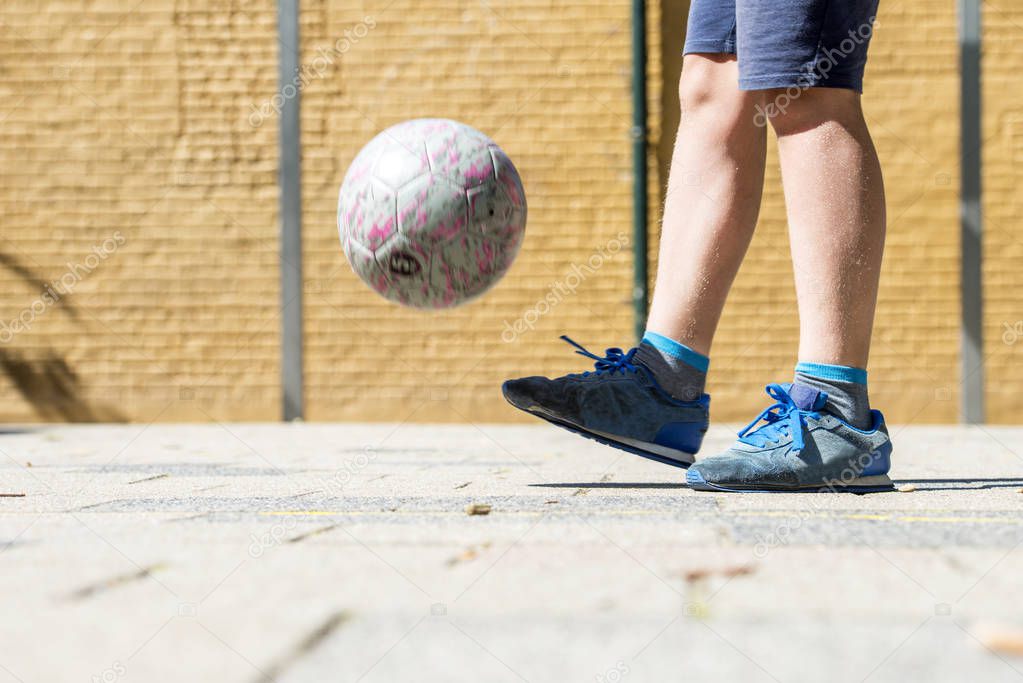 Boy wearing worn down sneakers keeping ball up on street soccer pitch